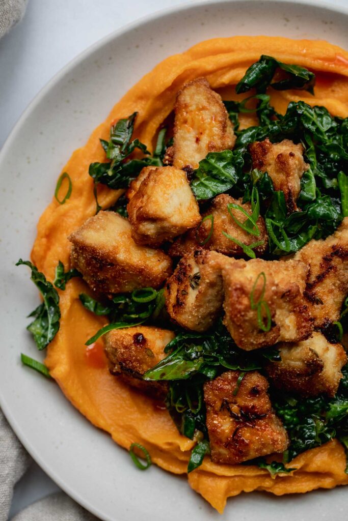 Close up of a plate of whipped sweet potatoes topped with kale and crispy tofu.