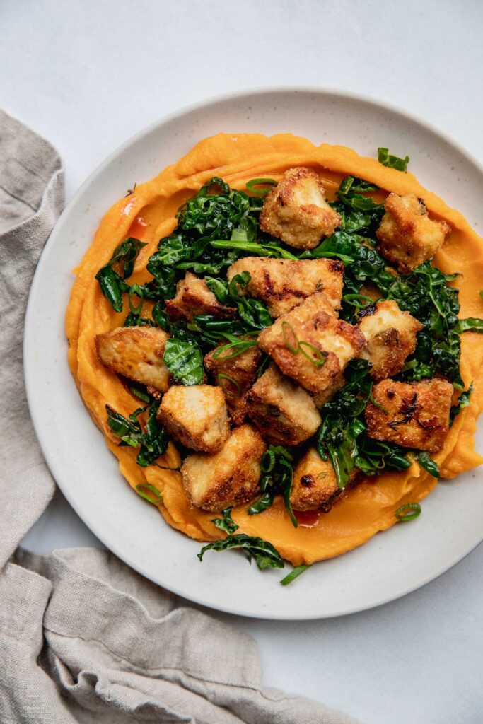 Plate with a spread of sweet potato puree topped with marinated kale and crispy tofu.