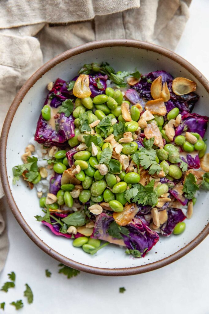 Bowl of rice topped with cabbage salad, edamame, garlic and peanuts.