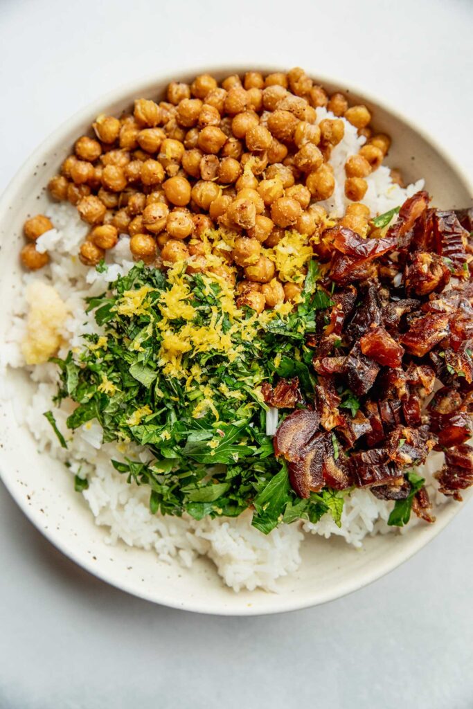 Rice in a bowl topped with roasted chickpeas, herbs, lemon, dates and garlic.