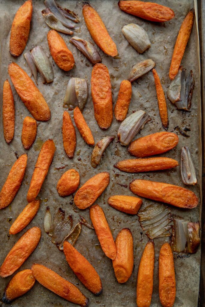 Roasted carrots and shallots on a baking tray.