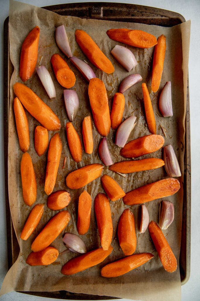 Seasoned carrots and shallots on a baking tray.