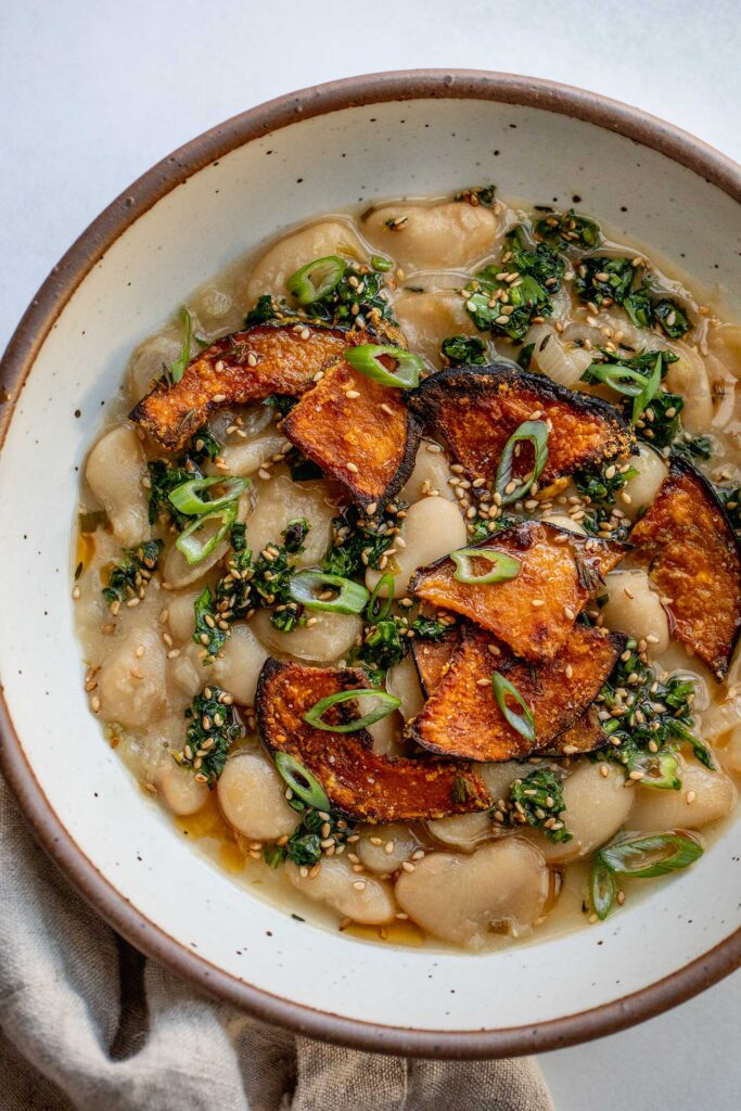 Bowl of creamy beans topped with sesame herbs and baked kabocha pieces.