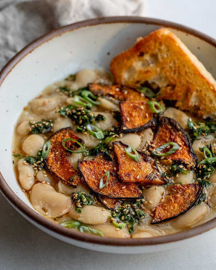 Bowl of creamy beans served with toasted bread and topped with sesame herbs and kabocha squash.