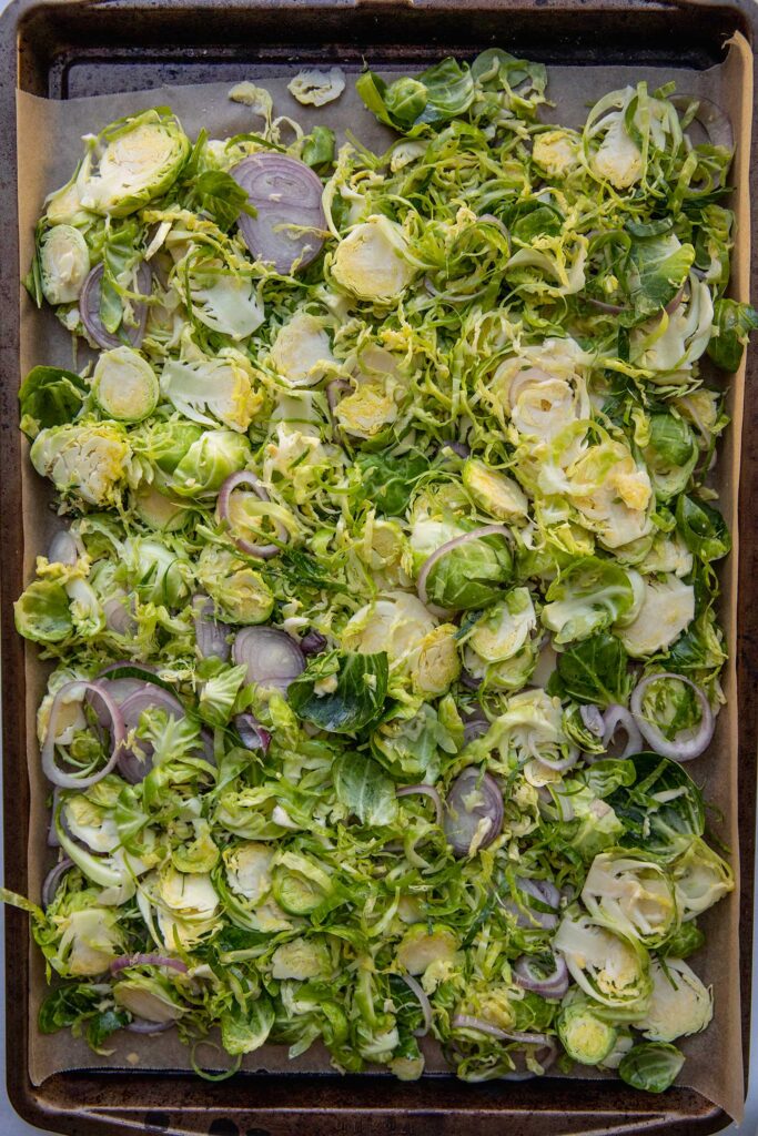 Seasoned shredded brussels sprouts and shallots on a baking tray.