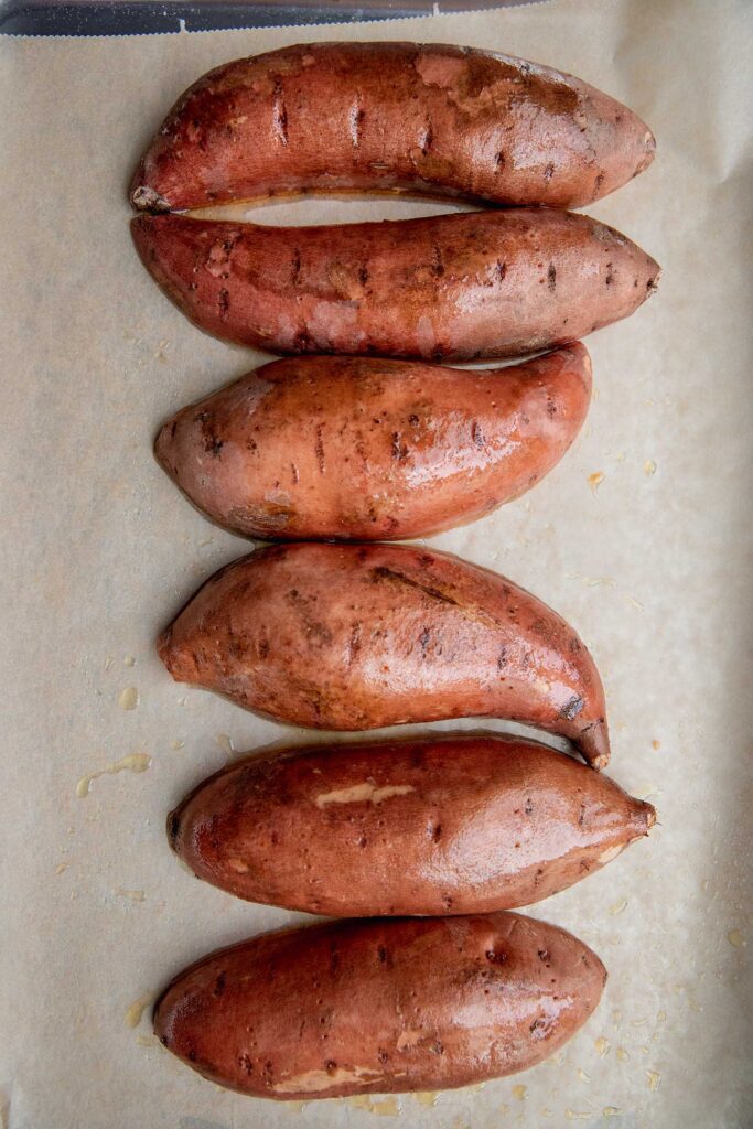 Halved sweet potatoes placed on a baking tray cut side down.