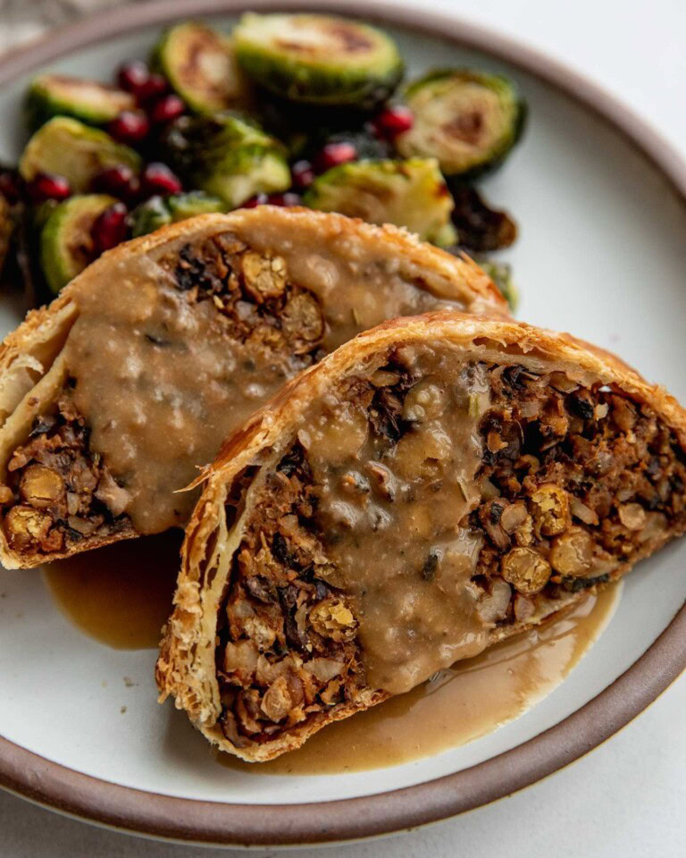 Serving two slices of the vegetable wellington with roasted brussels sprouts on a plate topped with gravy.