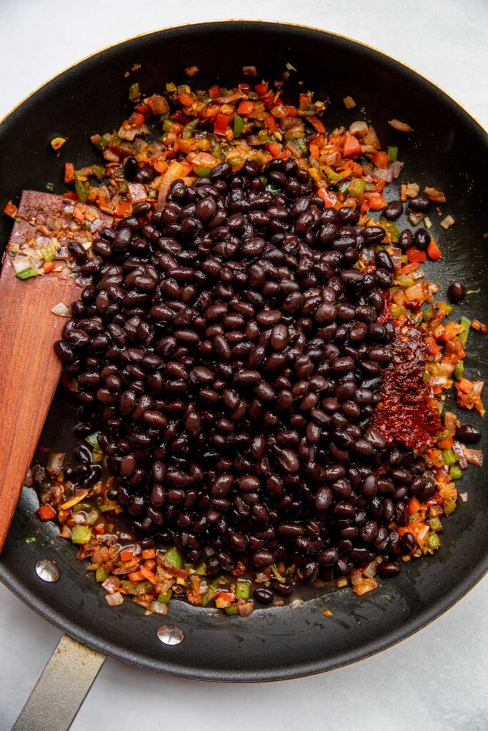 Stirring the black beans into the sautéed vegetables.