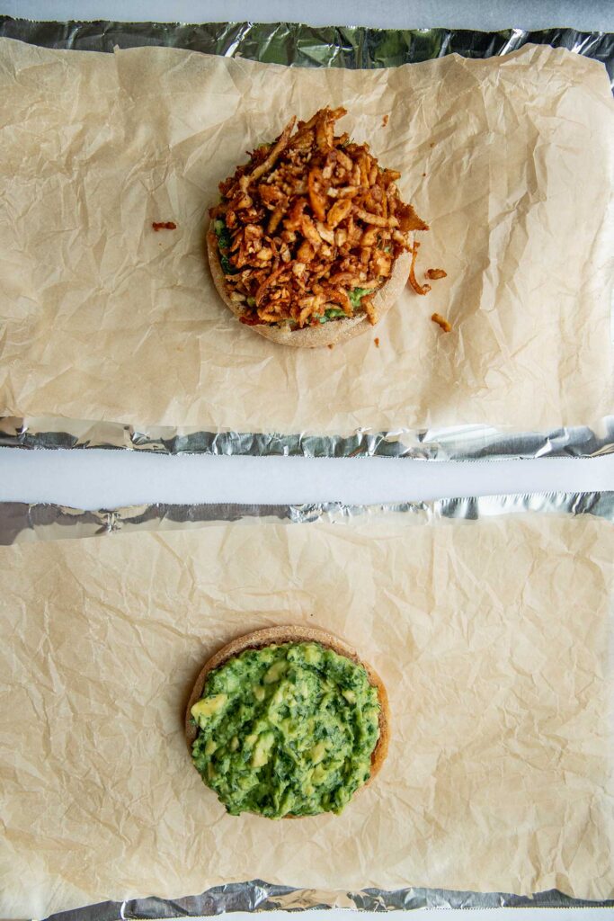 Process of assembling breakfast sandwiches showing one English muffin topped with avocado and another topped with avocado and the tofu shreds.