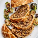 Sliced vegetable wellington on a plate with roasted brussels sprouts on the plate.