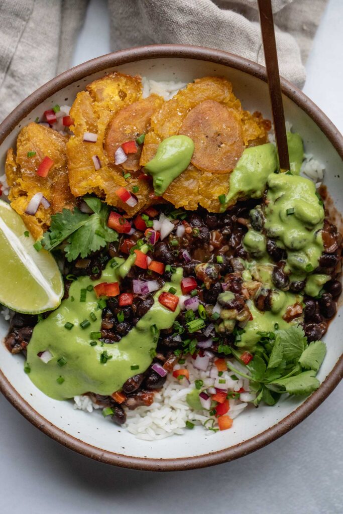 Grabbing a spoon of the rice and black beans covered in avocado cilantro sauce with plantains arranged on the side of the bowl.