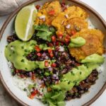 Bowl of rice topped with chipotle black beans and an avocado cilantro sauce with plantains arranged to the side.