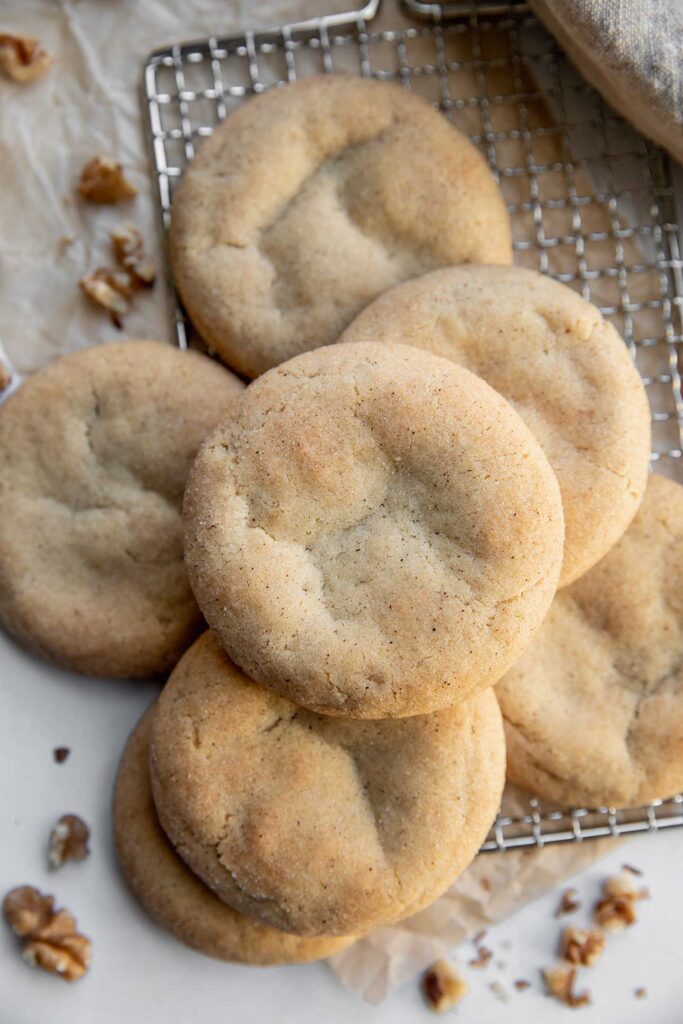 A pile of cookies surrounded by crush walnuts on parchment paper and a cooling rack.