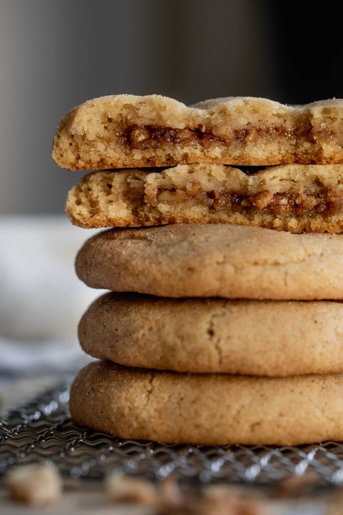 Close up of a stack of cookies with the cookie on top broken in half to show the brown sugar filling.