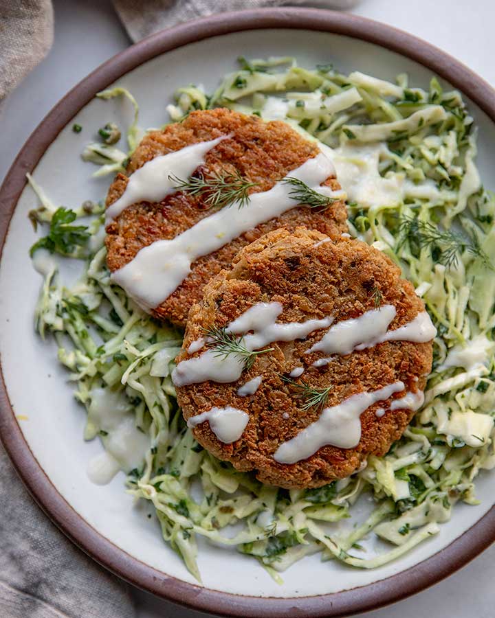 Close up of a plate of cabbage slaw topped with tofu patties drizzled with yogurt sauce.