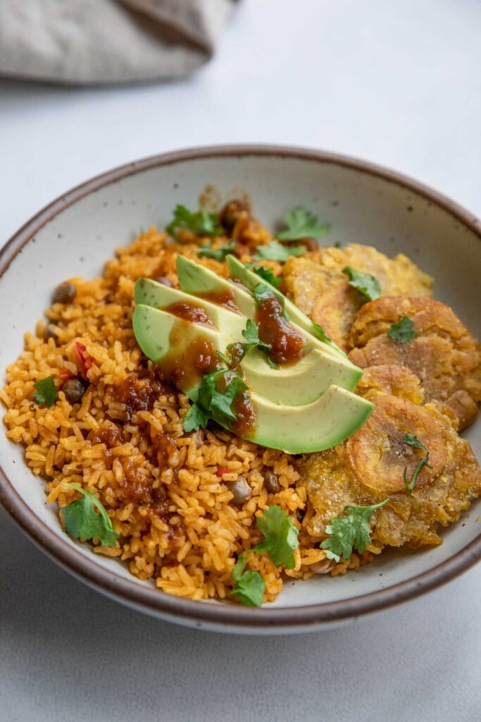 Topping a bowl of moro served with plantains with avocado, cilantro and hot sauce.