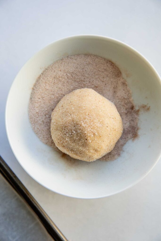 Rolling the stuffed cookie dough ball in a bowl of cinnamon sugar.