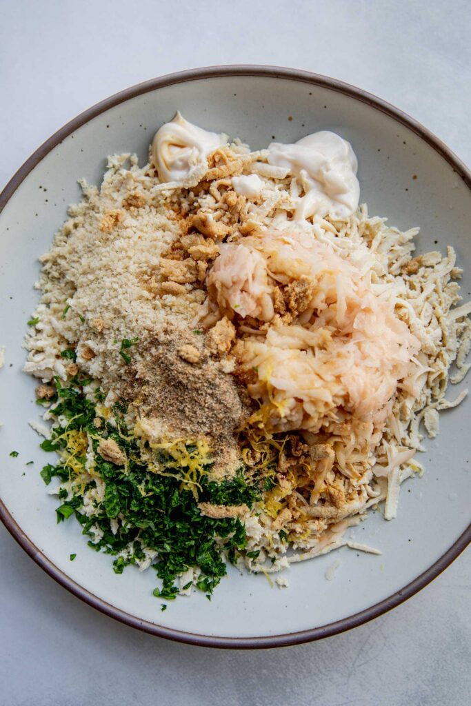 Mixing bowl filled with shredded tofu, potatoes, mayo, herbs, seasonings and lemon.