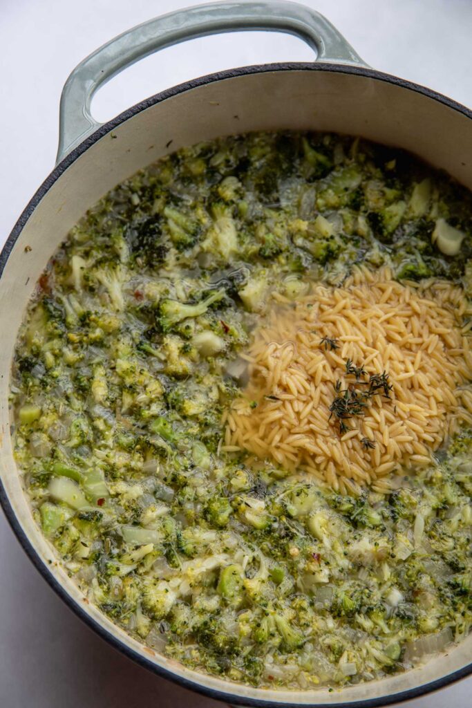 Adding orzo to a pot of broccoli soup broth.