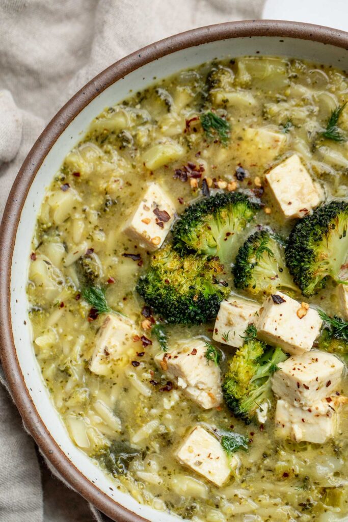 Large bowl of orzo soup topped with roasted broccoli ad tofu feta.