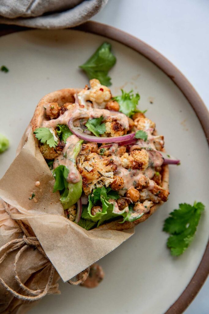 Top down view of a pita wrap on a plate stuffed with roasted cauliflower, chickpeas, lettuce and pickled onions.