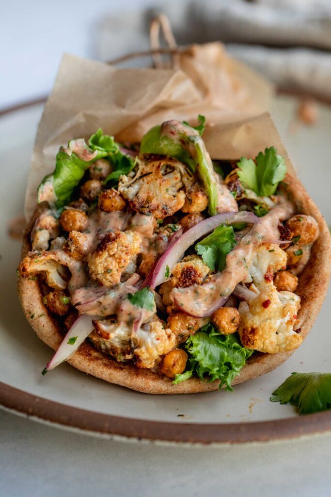 Close up of a pita wrap stuffed with charred cauliflower, chickpeas, pickled onions, lettuce and chipotle sauce.