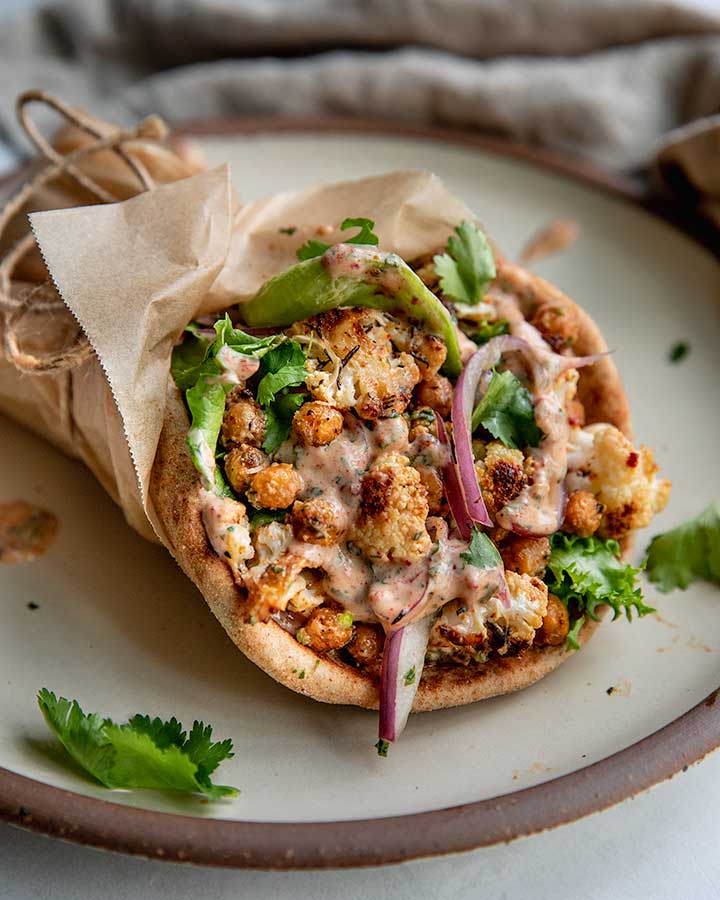 Pita wrap on a plate filled with chickpeas, cauliflower, pickled onions, lettuce and chipotle sauce.