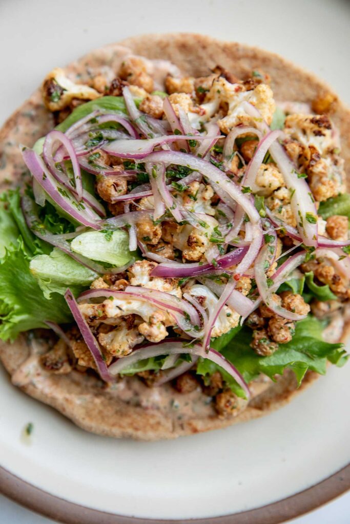 Wrap layered with chipotle sauce, lettuce, cauliflower, chickpeas and pickled onions.