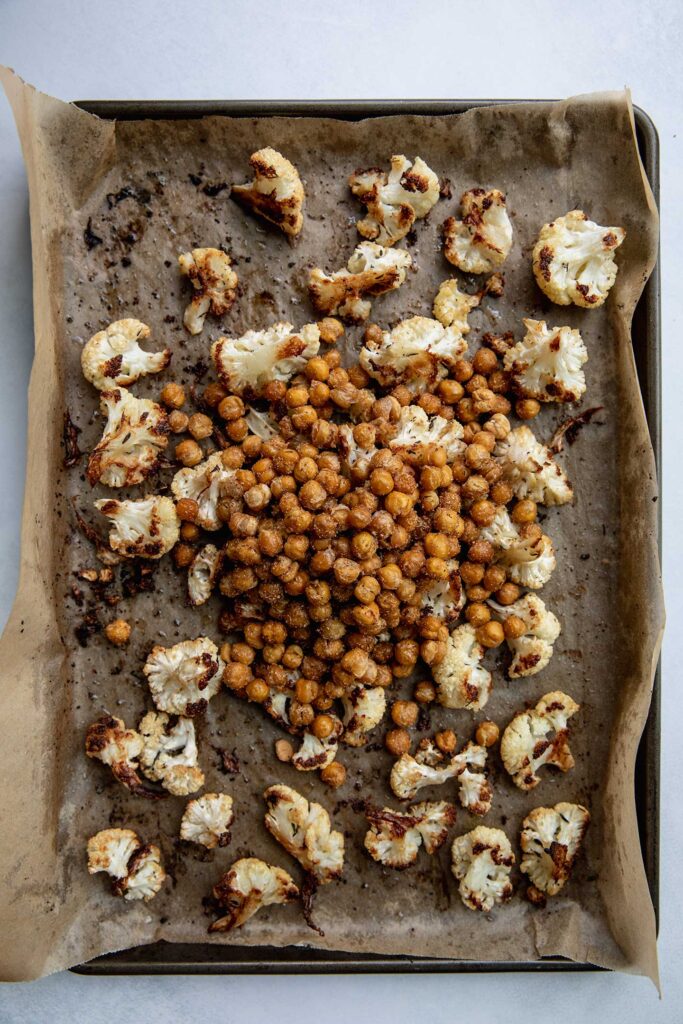 Transferring roasted chickpeas to a baking tray of charred cauliflower.