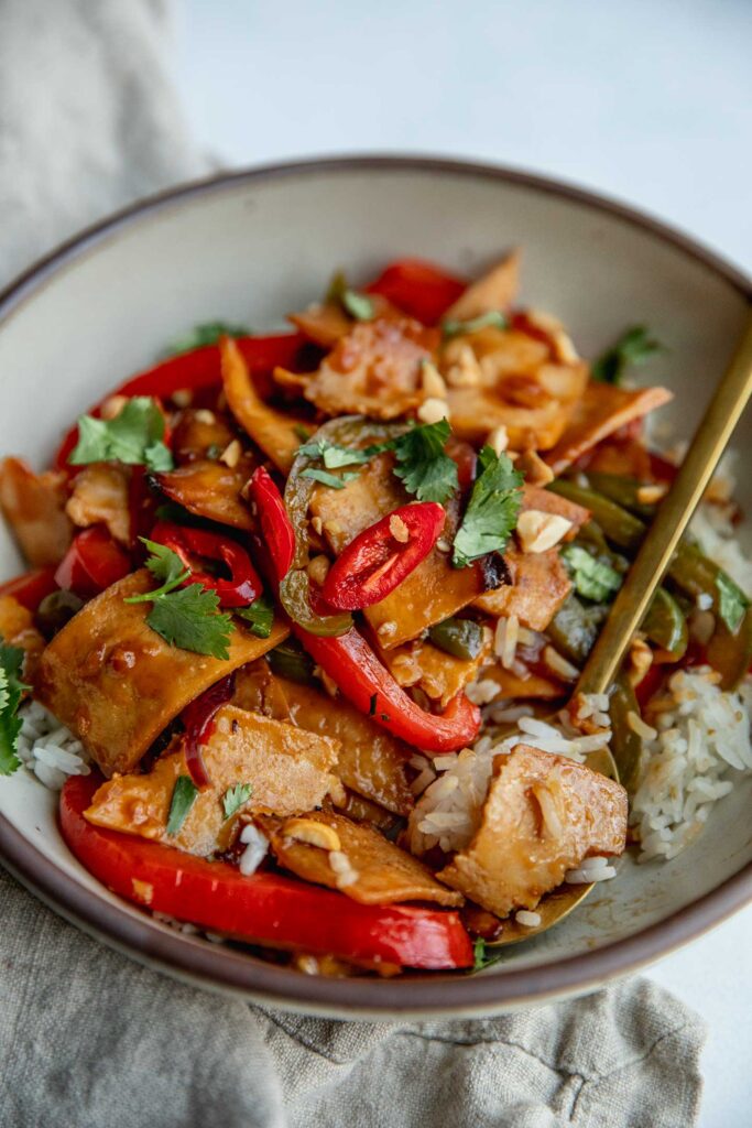 Eating from a bowl of tofu and pepper stir-fry with rice using a gold spoon.