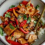 Bowl of rice served with stir-fried peppers and tofu and topped with cilantro and peanuts.