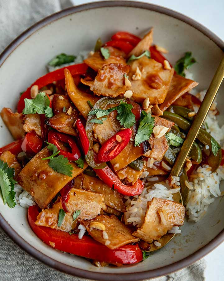 Bowl of rice served with stir-fried peppers and tofu and topped with cilantro and peanuts.