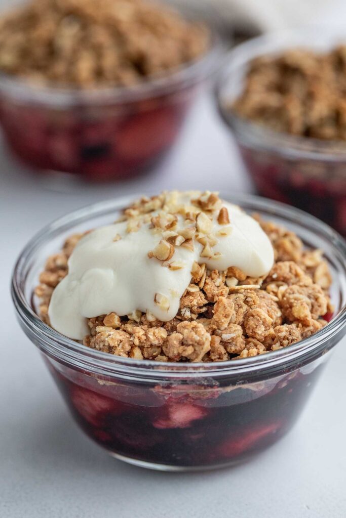 Three small baking dishes filled with berries and topped with an oat crumble and yogurt.