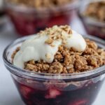 Close up of a small baked berry crumble topped with yogurt and chopped pecans.