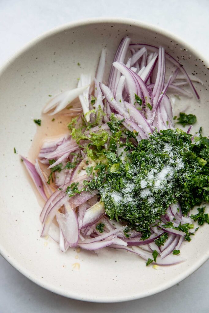 Sliced red onions, cilantro, onions, lime zest and juice in a bowl.