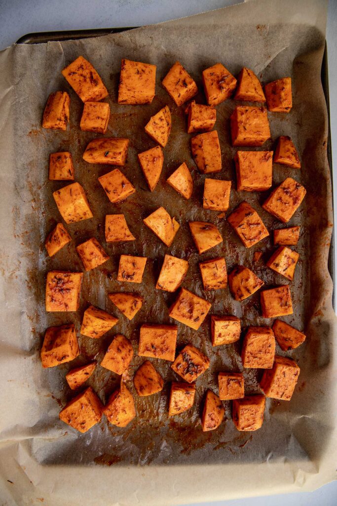 Seasoned cubed sweet potatoes on a parchment lined baking tray.