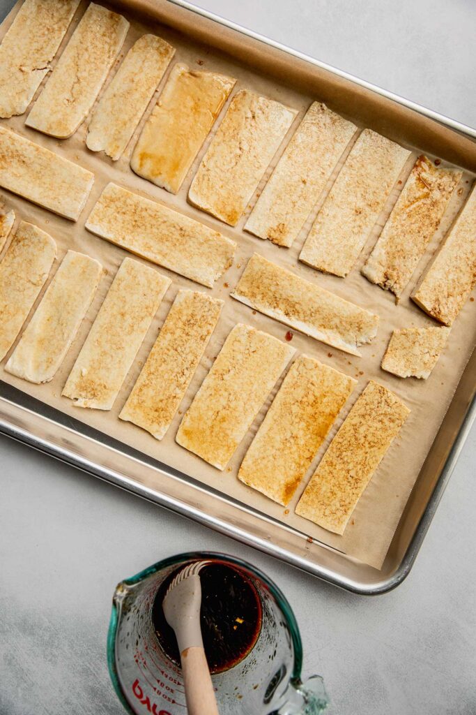 Tofu strips coated in soy sauce marinade on a baking tray.