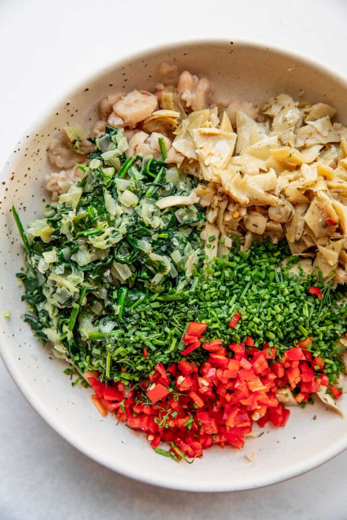 Bowl filled with mashed white beans, artichoke hearts, sauteed spinach, pepper, and fresh herbs.