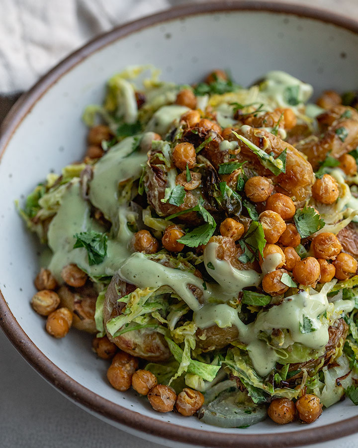 Side view of a baked shredded brussels sprout salad tossed together with roasted potatoes, chickpeas and avocado dressing.