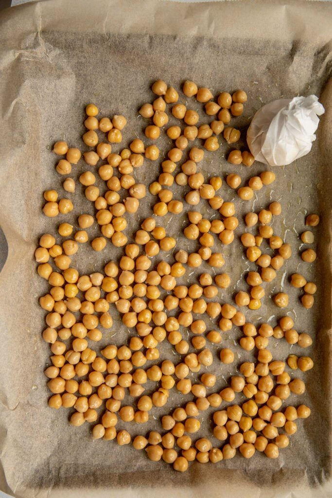 Tray with oiled chickpeas and garlic cloves wrapped in parchment paper.