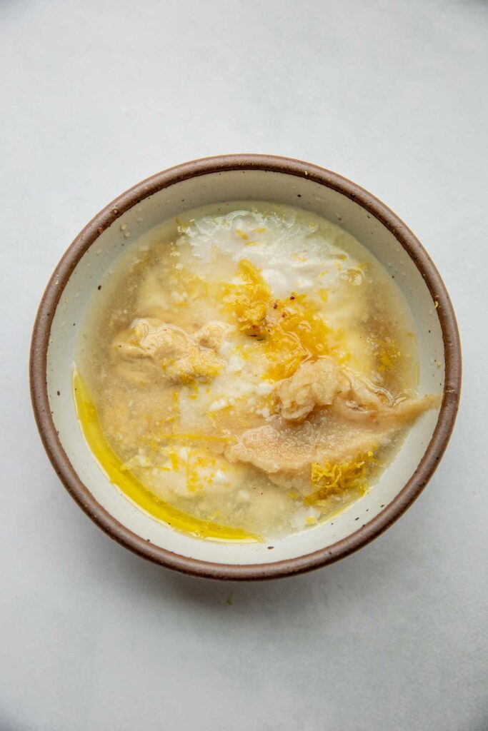 Maple syrup, yogurt, Dijon mustard, lemon and roasted garlic in a small white bowl.