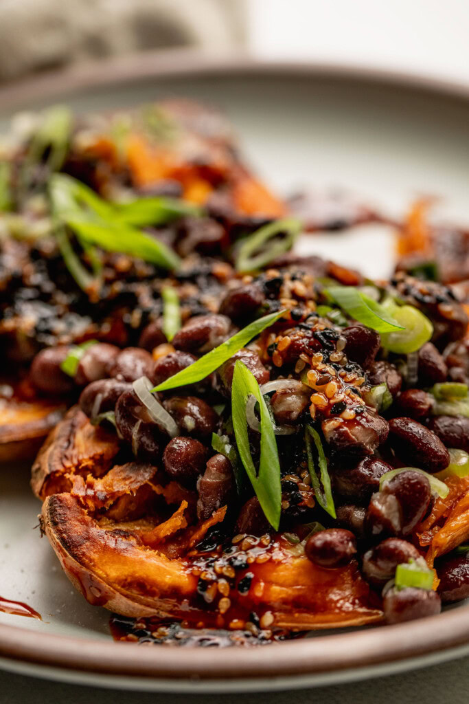 Close up of a baked sweet potato half stuffed with black beans, gochujang sauce and scallions.