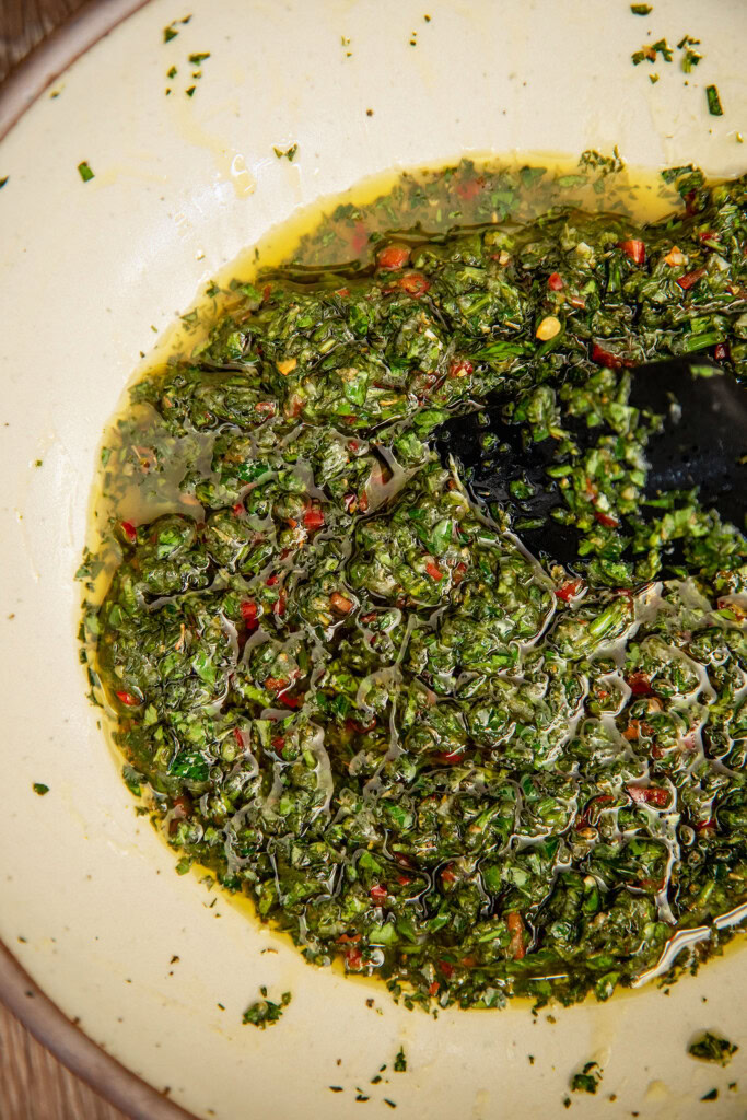 Chimichurri sauce being mixed together in a bowl with a spatula.