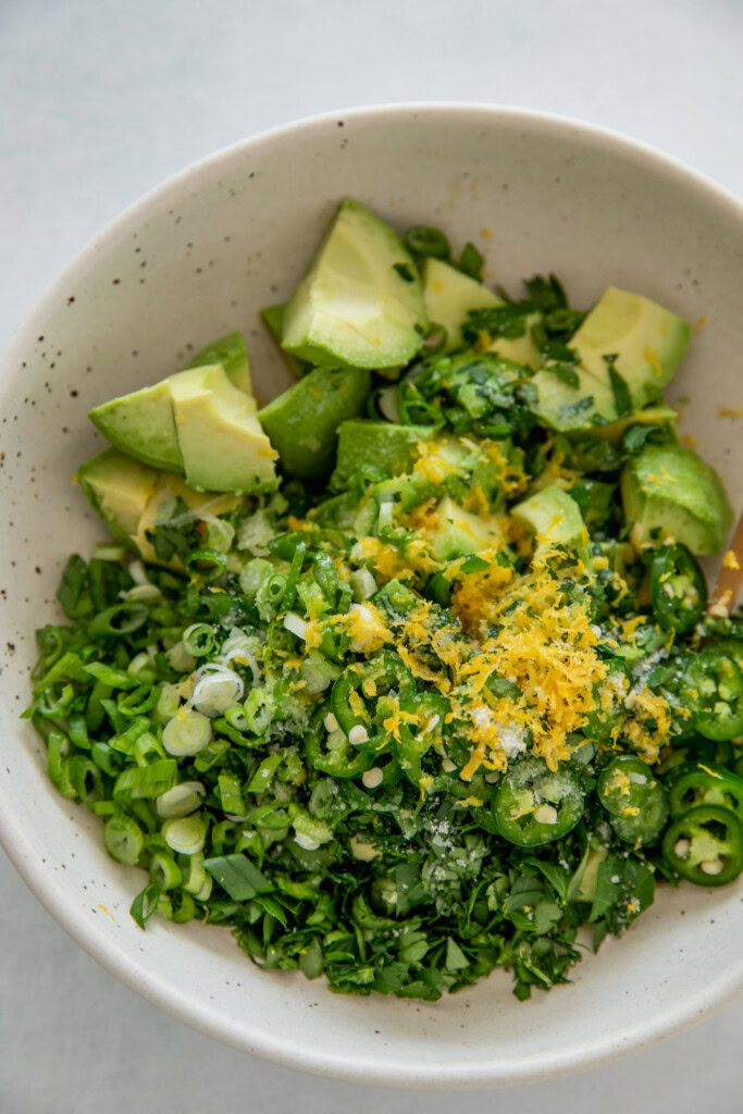 Schüssel mit Avocadowürfeln, Petersilie, Frühlingszwiebeln, Pfeffer, Zitronenschale und Salz gefüllt.