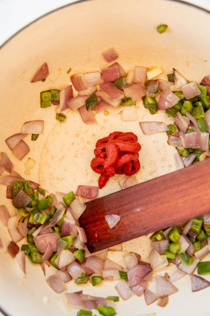 Adding tomato paste to a pot of sauteed onions and jalapeno.