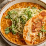 Close up of a bowl of creamy red lentils topped with cabbage slaw and a piece of a crispy scallion pancake on top.