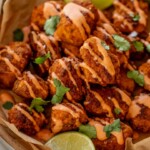 Close up of a plate of pica tofu on top of parchment paper and covered in a drizzle of mayo ketchup. Served with lime wedges.