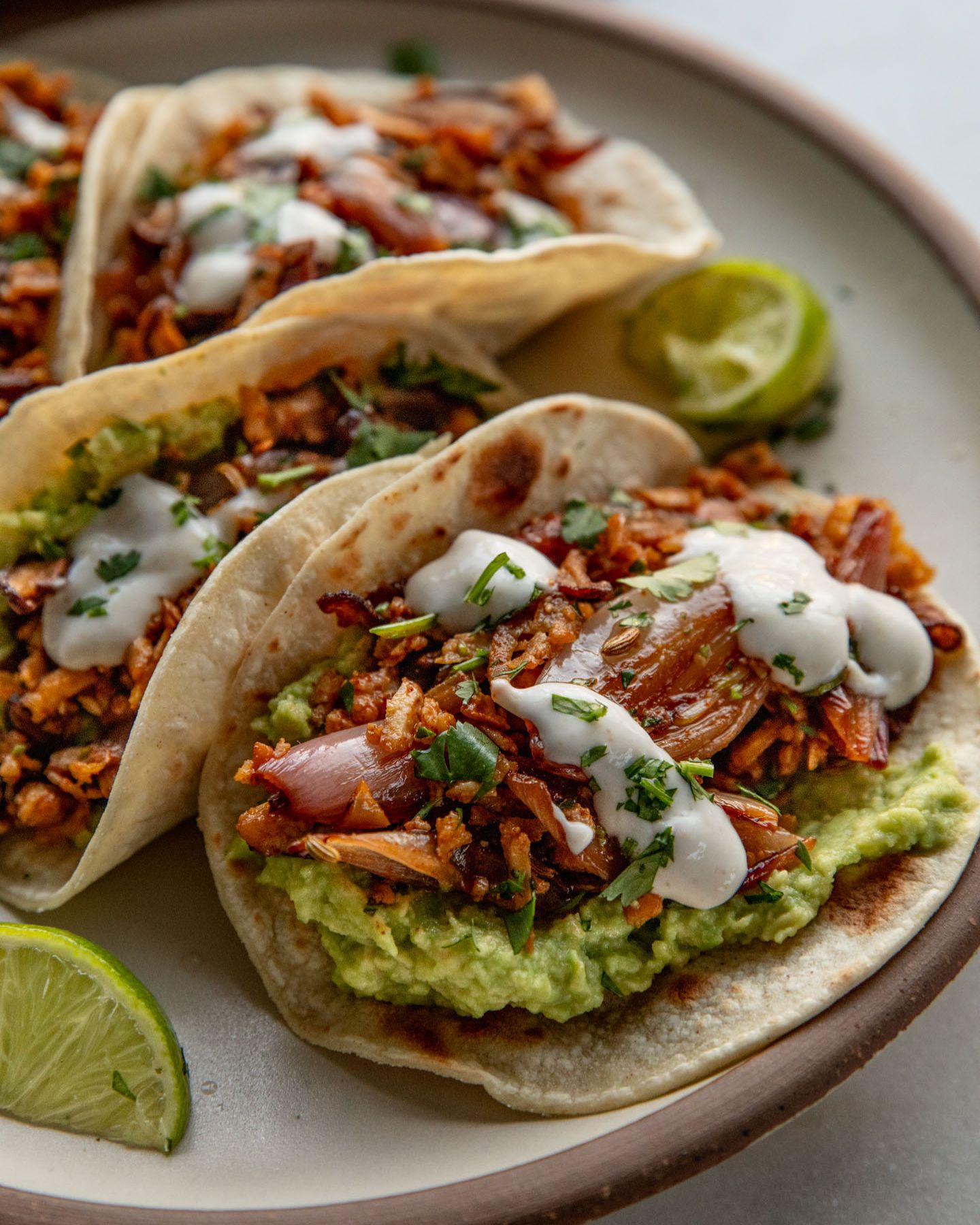 Side view of a plate of tacos filled with mashed avocado, shredded tofu topped with crema.