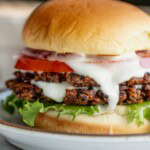Smash black bean burger layered in a bun with lettuce, toum, tomato, and pickled onions.