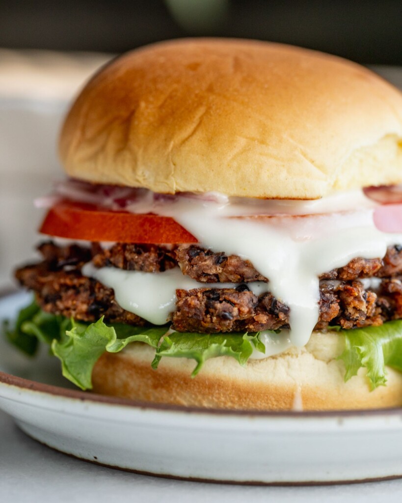 Smash black bean burger layered in a bun with lettuce, toum, tomato, and pickled onions.